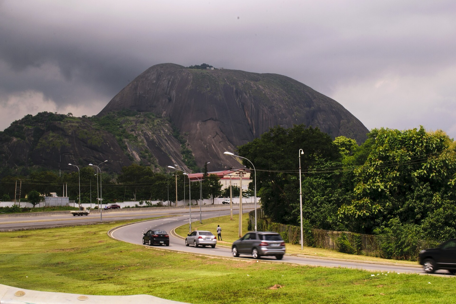 Aso Rock rising above a highway and trees in Abuja under a cloudy sky